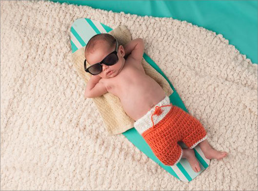تصویر با کیفیت از نوزاد ریلکس خوابیده روی اسکیت چوبی در ساحل