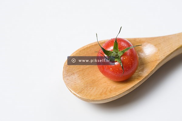 عکس با کیفیت از گوجه قرمز روی قاشق چوبی
