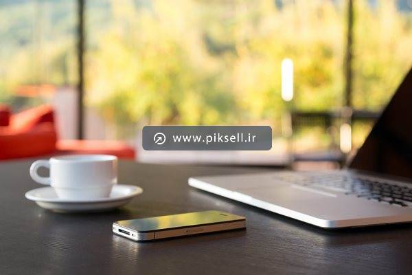 عکس با کیفیت از نمای تار طبیعت و لپ تاپ ، گوشی و فنجان قهوه روی میز کار