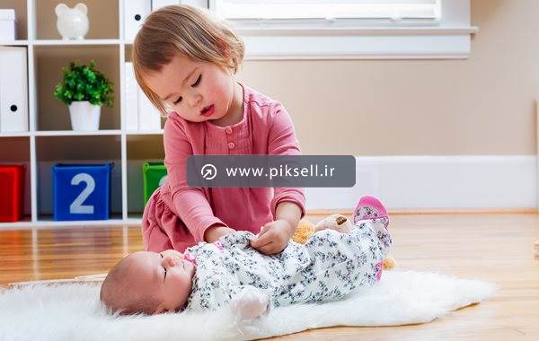 تصویر با کیفیت از دختر کوچولو در حال پوشاندن پیراهن به نوزاد
