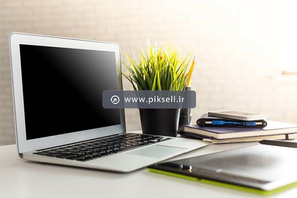 عکس با کیفیت از نمای میز کار و ابزارهای لپ تاپ ، گلدان و قلم نوری و دفترچه