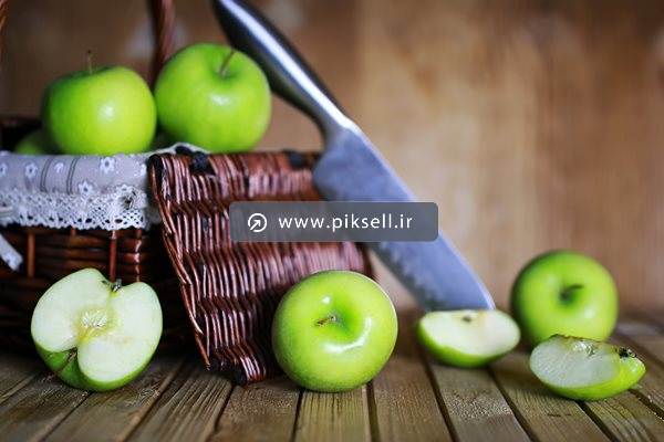 دانلود عکس با کیفیت از سیب های سبز و سبد حصیری و چاقو