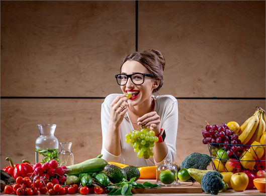 تصویر با کیفیت از میوه و صیفی و سبزیجات و دختر جوان در حال خوردن انگور