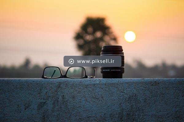 تصویر با کیفیت از عینک و لنز دوربین و بکگراند غروب خورشید