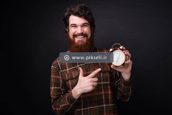عکس با کیفیت از مرد ریش دار در حال اشاره به ساعت شماطه دار