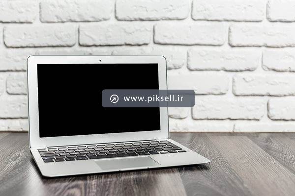عکس با کیفیت از مک بوک قدیمی روی میز چوبی با دیوار آجری