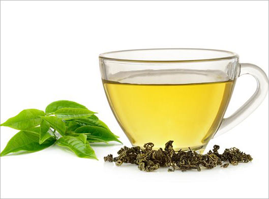 عکس با کیفیت از دمنوش در فنجان شیشه ای و برگهای سبز