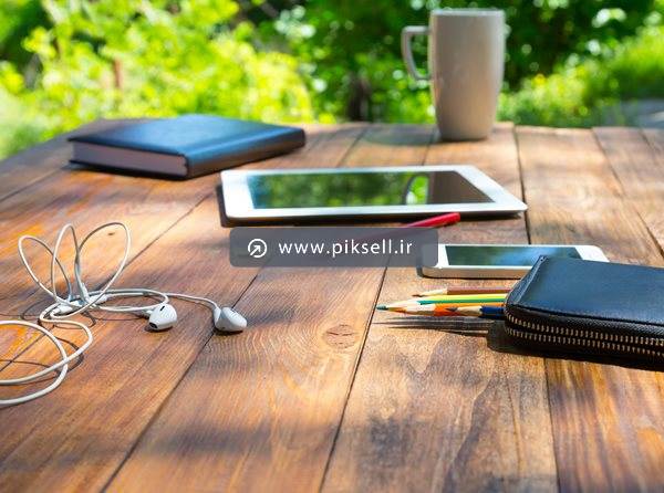 عکس با کیفیت از میز کاری و تبلت و کتاب و هدفون و گوشی روی میز چوبی