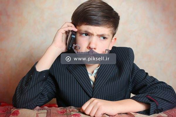 تصویر با کیفیت از پسر بچه با سبیل مصنوعی و تلفن همراه