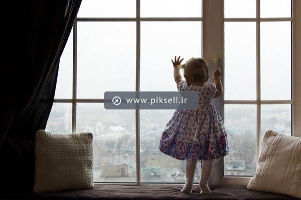 عکس با کیفیت از دختربچه پشت پنجره و نمای شهر